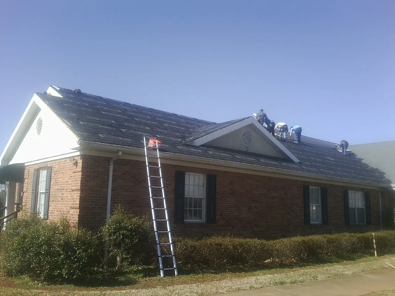 Crew tearing shingles off a brick ranch roof with a ladder set — Metal Roof Repair work by our crew in Chandlersville