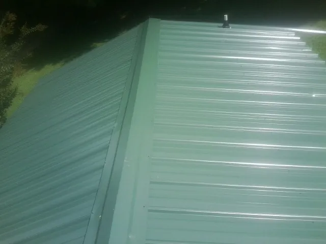 New green metal panels meeting at the ridge of a roof — Flat Roof Repair work by our crew in Chandlersville