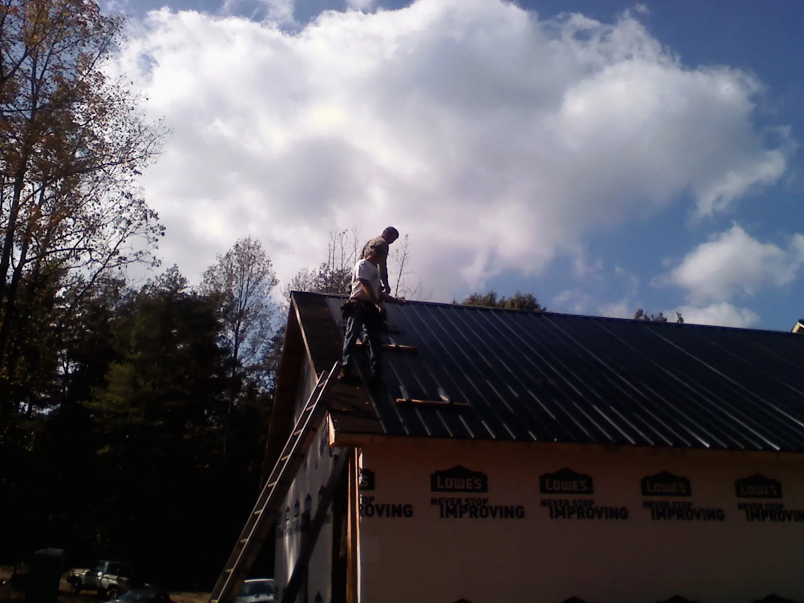 Roofer fastening dark metal panels high against a cloudy sky, from a Roof Inspection job in Chandlersville