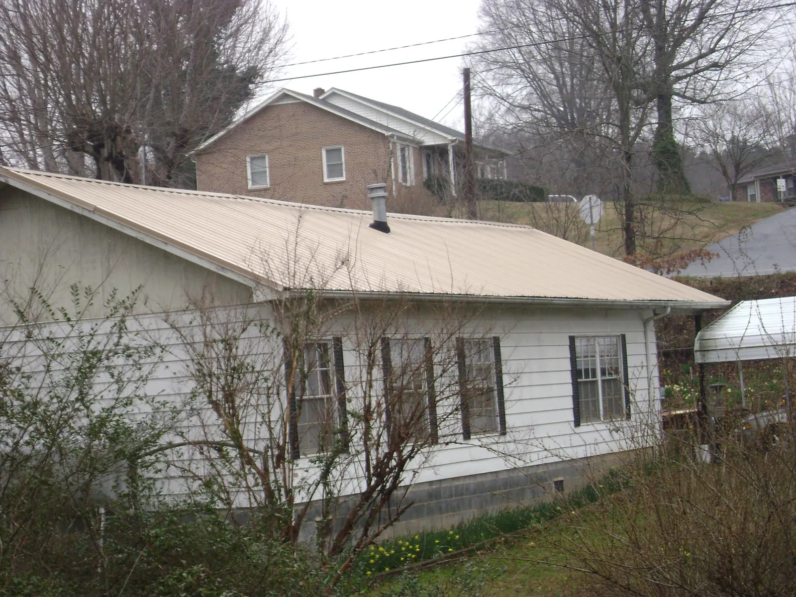 Tan metal roof on a white sided house set into a hillside — Commercial Roofing by Roofing Brothers in Chandlersville